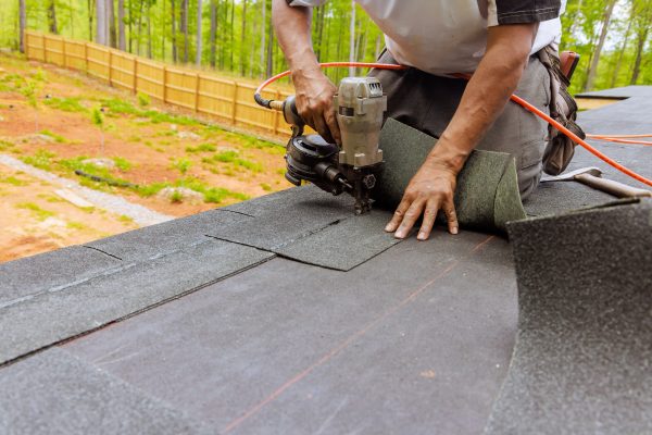 Installation of new asphalt bitumen shingles using an air pneumatic nail gun by roofer