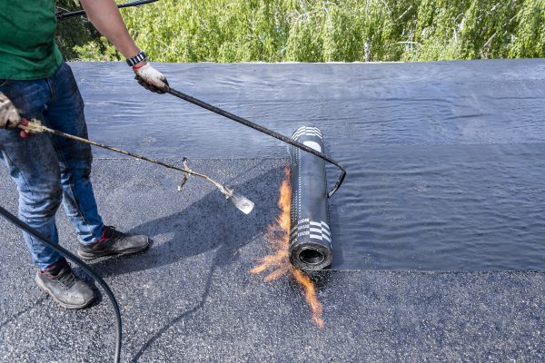 The builder puts waterproofing material on the roof of a multi-story residential building using a gas burner. Overhaul of the roof of the house.